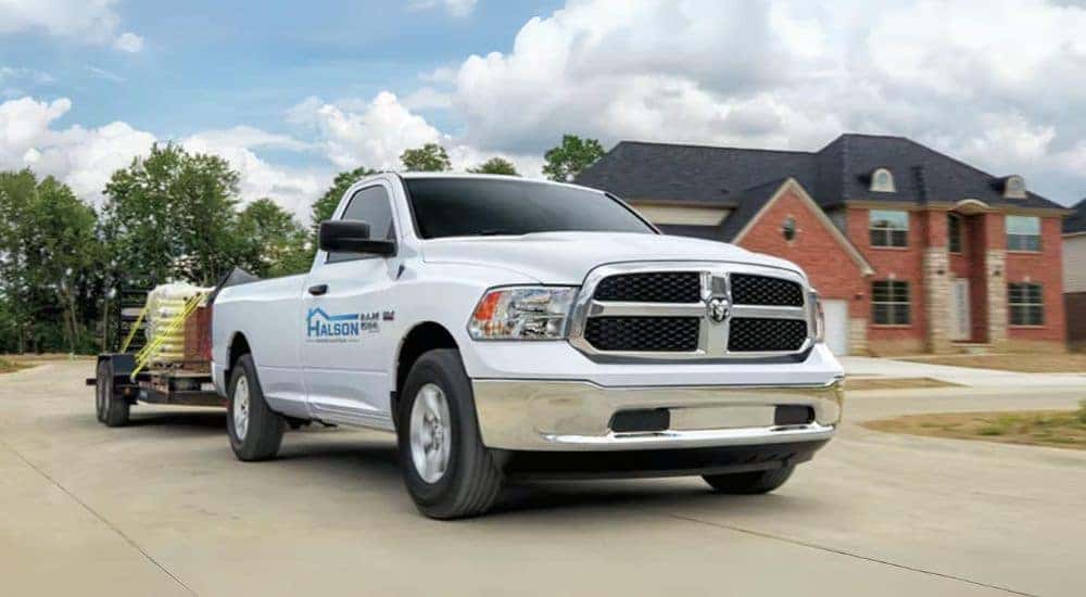 A white 2023 Ram 1500 Classic is shown towing a utility trailer.