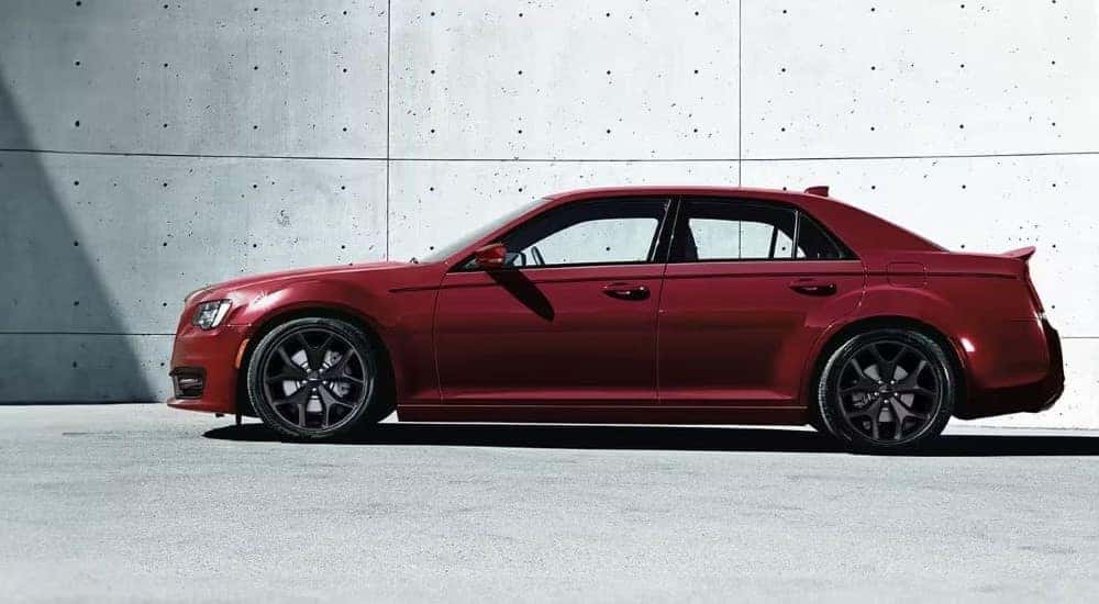 A side angle view of a red 2024 Chrysler 300 parked by a concrete wall.