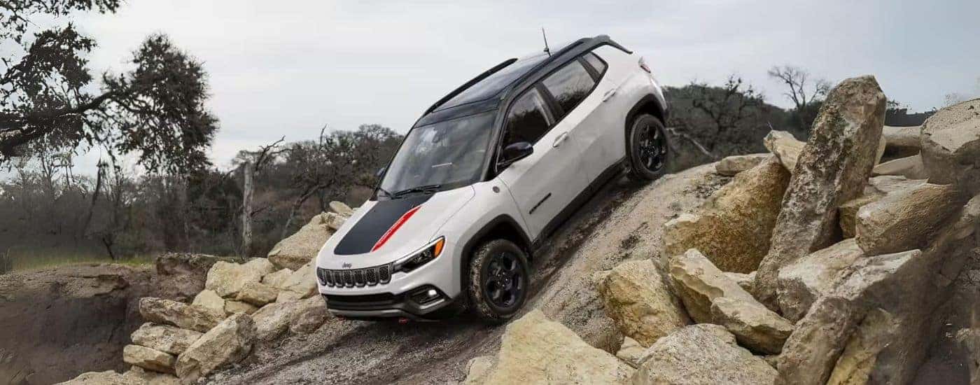 A white 2023 Jeep Compass Trailhawk is shown driving down a hill.