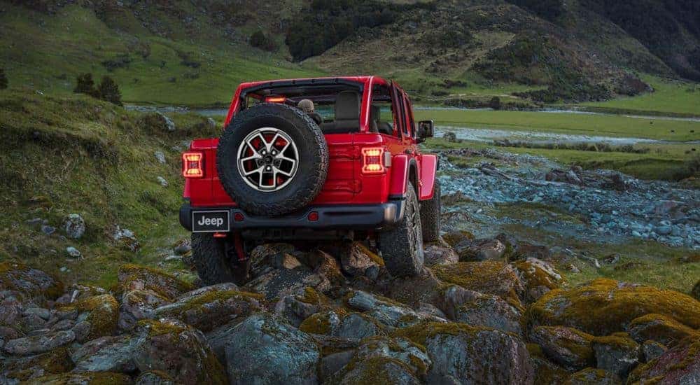 A red 2024 Jeep Wrangler for sale is shown from the rear off-road.