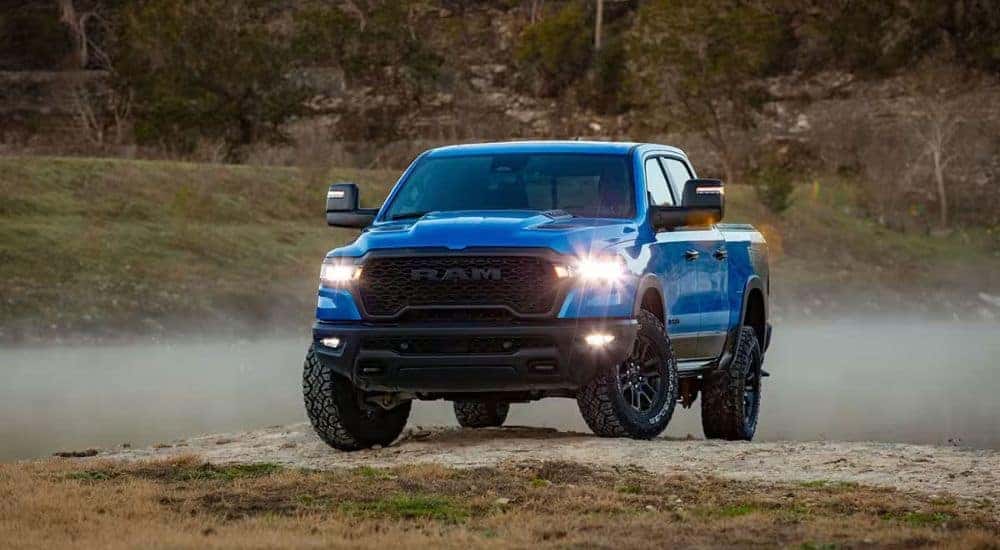 A blue 2025 Ram 1500 for sale is shown from the front parked off-road.