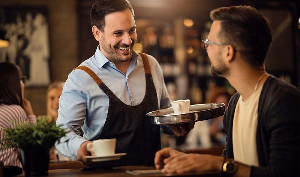 Genesis Of Northampton Dealership near Hadley, MA | Server bringing coffee to the table while smiling
