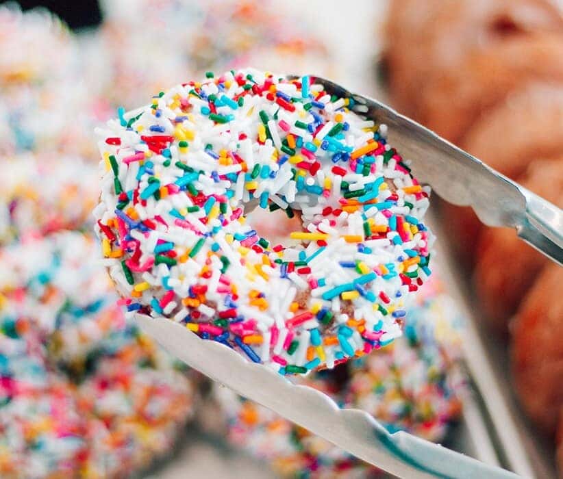 Genesis Dealership near Westfield, MA | Donut Shop Worker Picking up a Vanilla Sprinkle Donut with Large Tongs