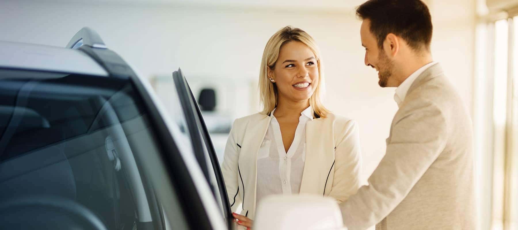 car salesman shows woman new car in showroom