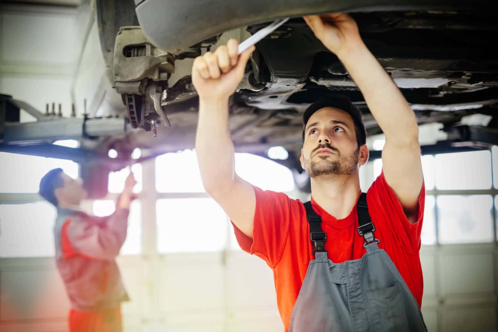 Mechanic in Red Shirt Working on Underside of Car