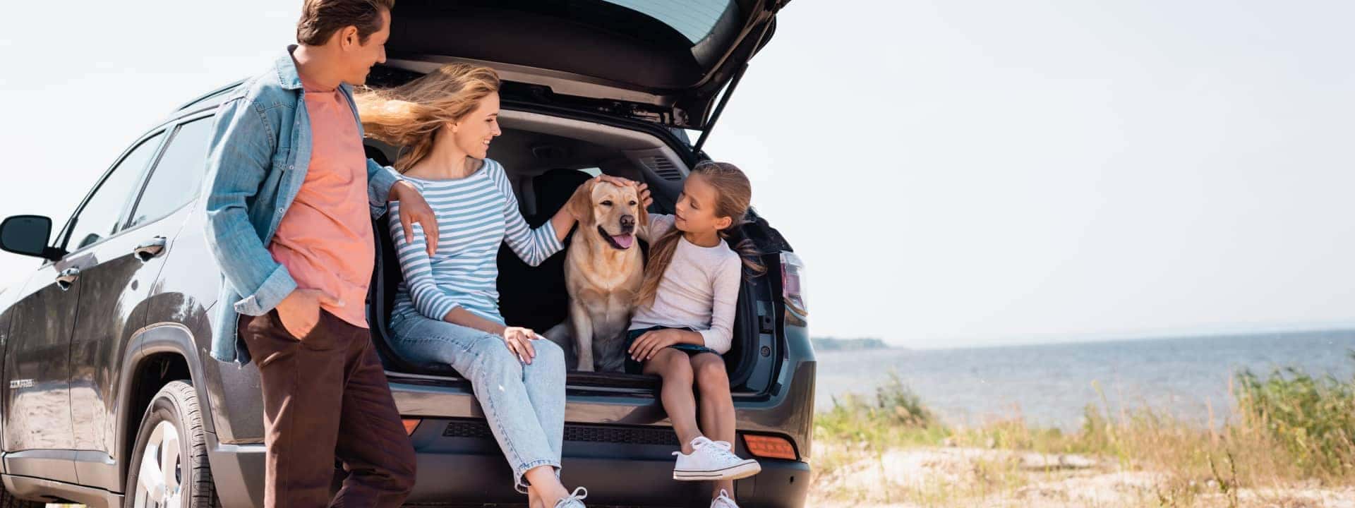Family with a dog sitting in the back of an SUV