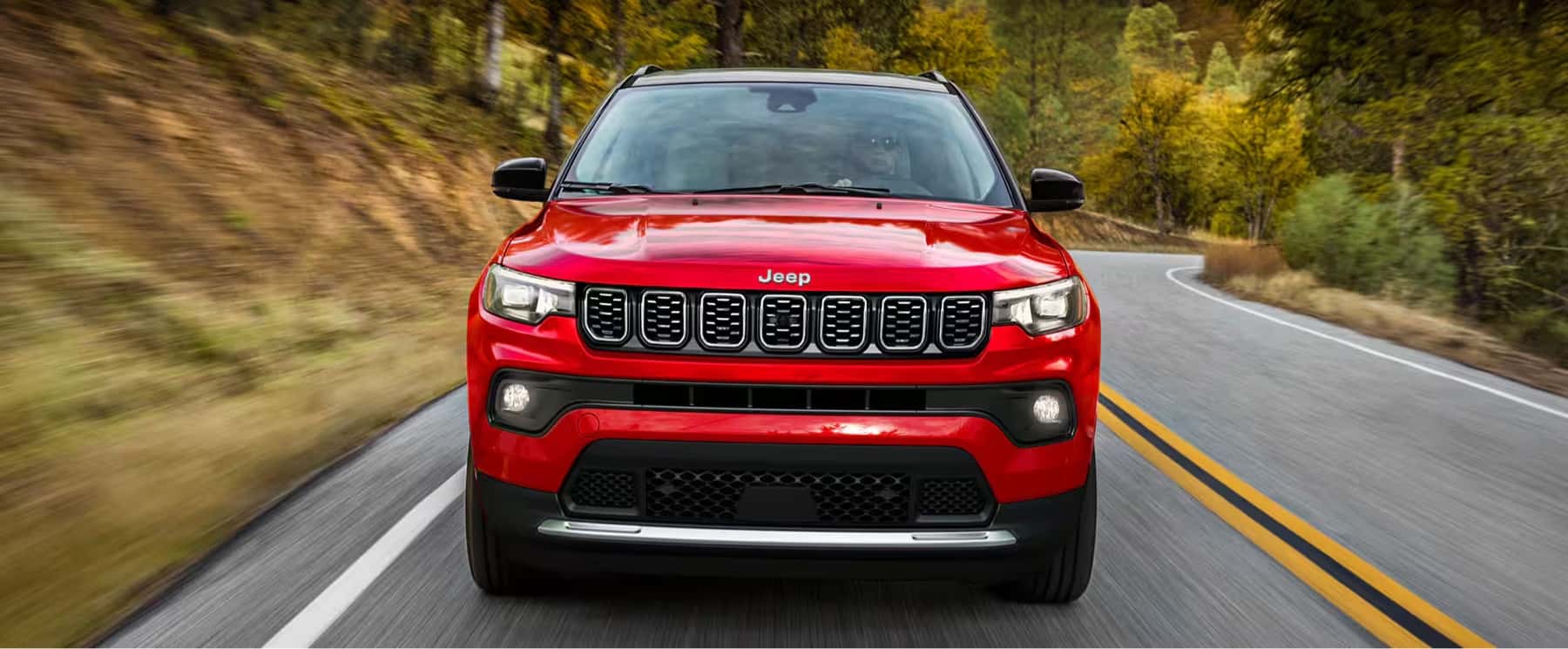2025-Jeep-Compass-speeding-down-a-forested-mountain-road