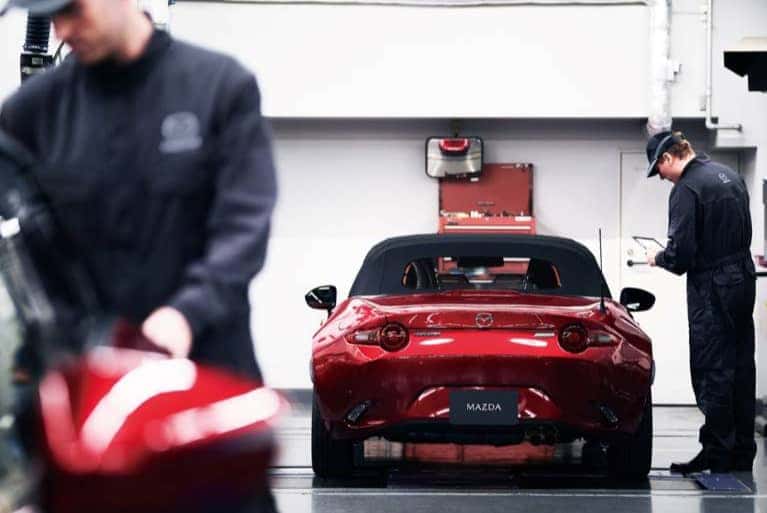 Mazda-service-technician-looking-at-a-clipboard-while-standing-by-a-red-vehicle