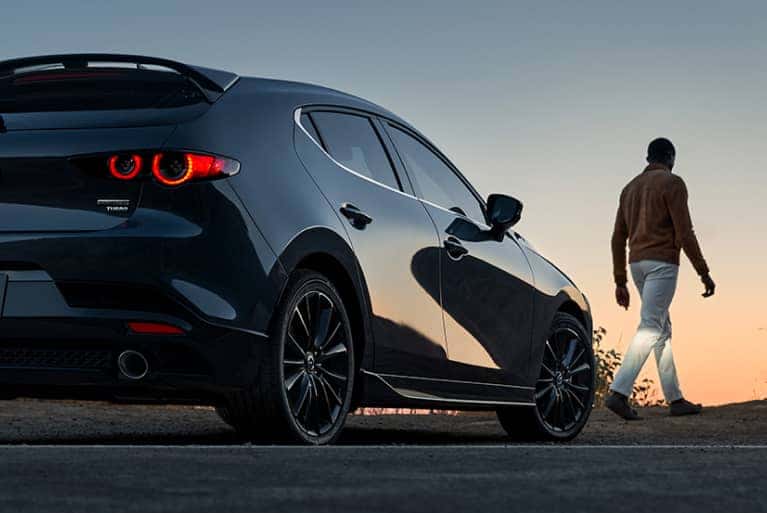 Rear-view-of-a-2024-Mazda3-Hatchback-at-sunset-with-a-person-walking-away-from-the-vehicle