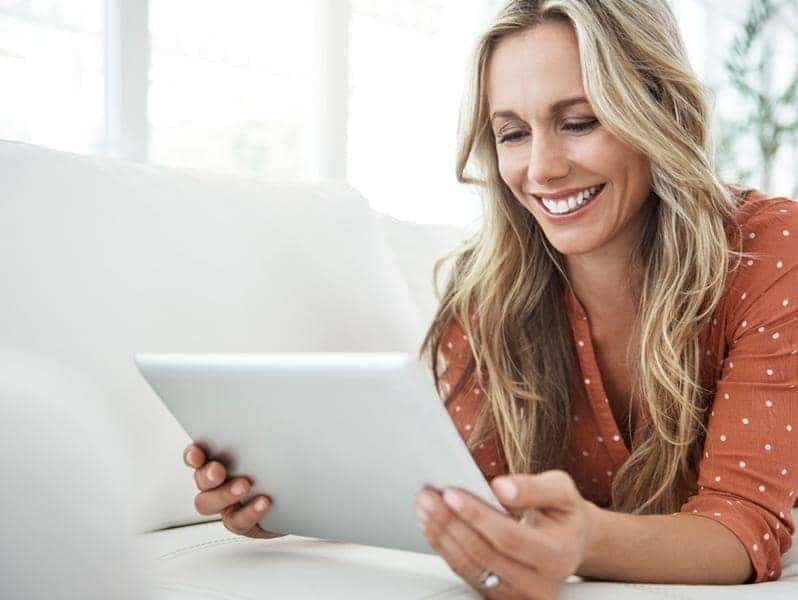 Woman shopping online from a tablet while lying on her sofa.