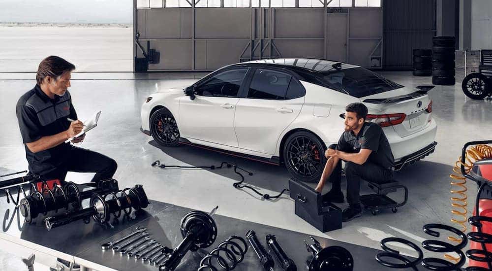 A white 2022 Toyota Camry TRD is shown being worked on in a mechanic's shop.