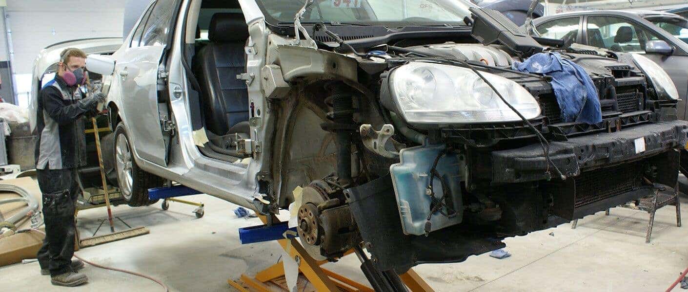 body shop technician sands car with facemask on
