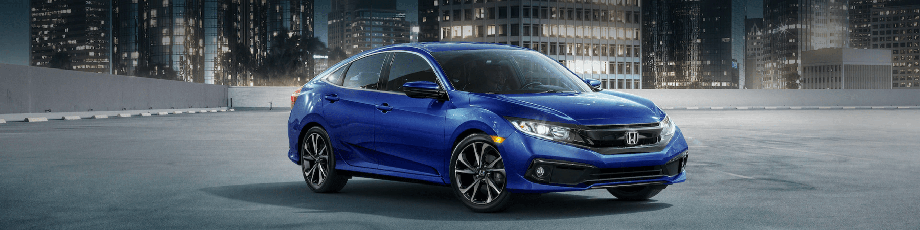 2021-Honda-Civic-Sedan-in-an-empty-parking-lot-in-front-of-an-urban-cityscape-at-night-slim