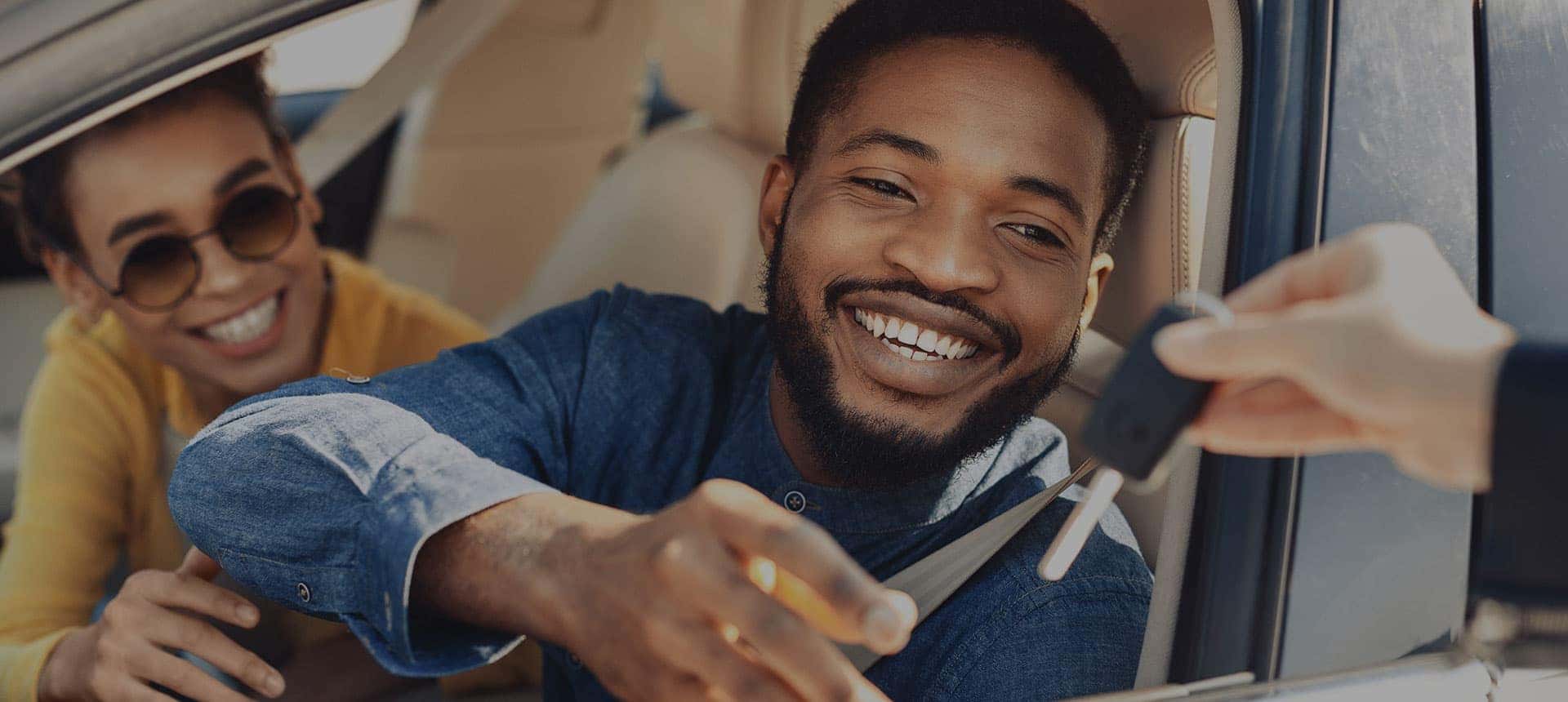 Man sitting in the driver's seat of his new car while being handed keys