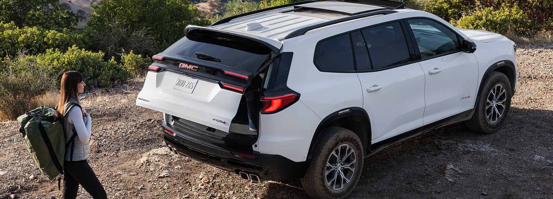 2026 GMC Acadia parked on dirt road woman with backpack