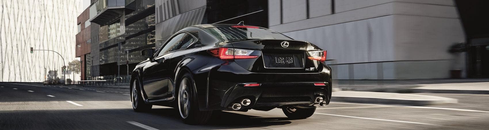 A close up of the back of a sleek black Lexus sedan as it speeds down a uncrowded city street.