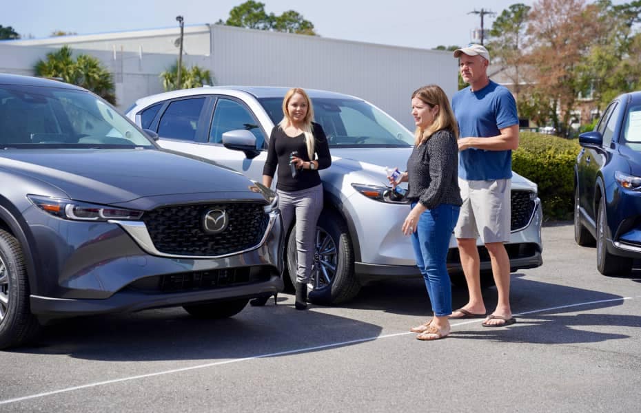 A sales representative showing off a new Mazda to a couple in the dealership lot