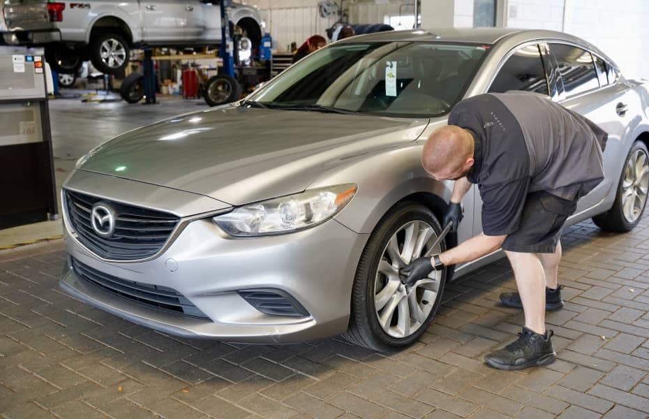 Mazda Service Tech inspecting front tire of vehicle inside of the service bay 