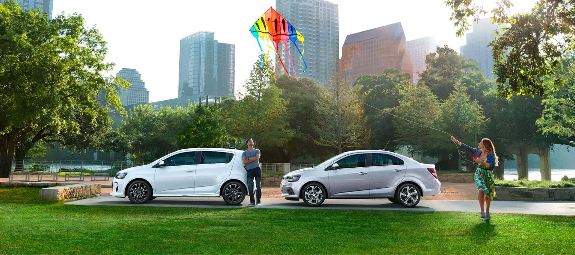 Man and woman are flying kites in a park next to their Chevrolet