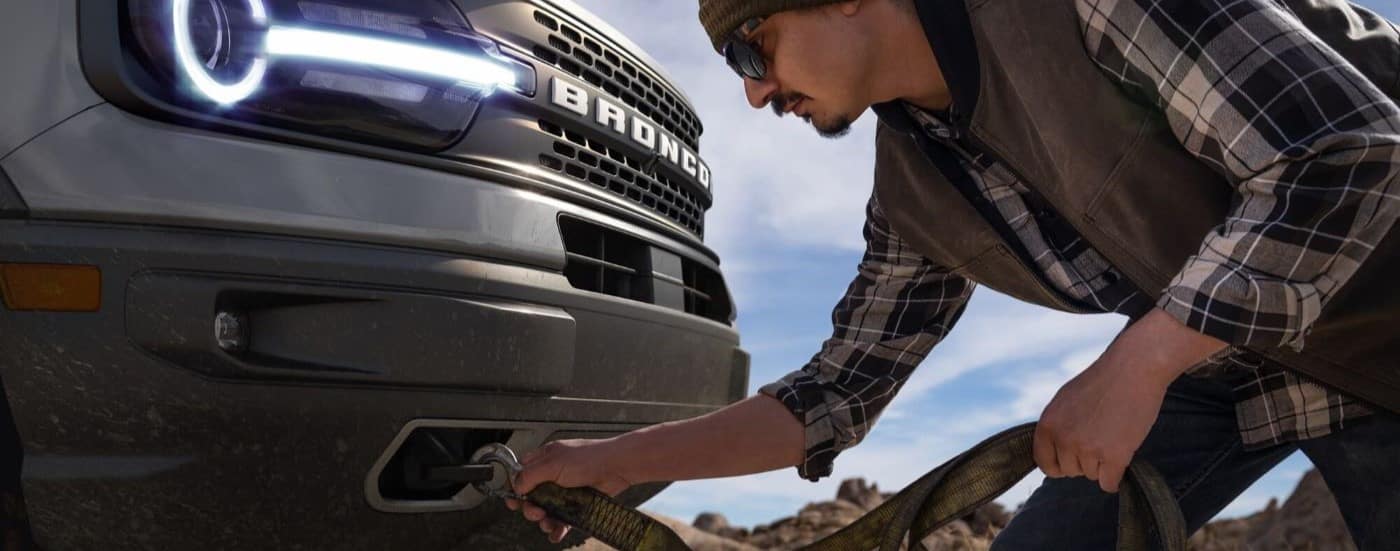 A person is shown hooking up a strap to the tow hook on a grey 2021 Ford Bronco Sport Badlands.