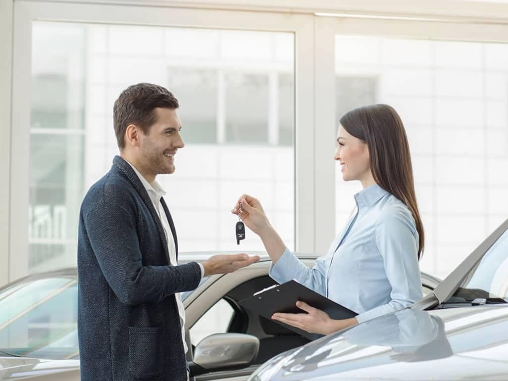 saleswoman is handing car keys to man inside showroom