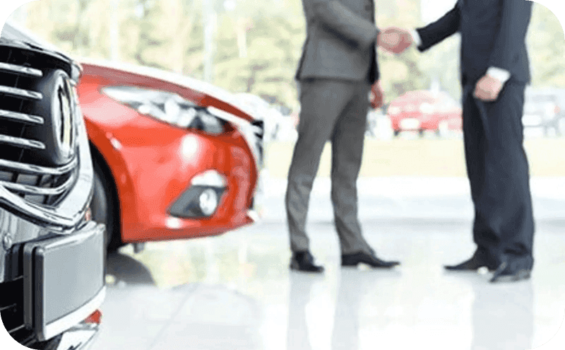 Two men in suits in a dealership showroom shaking hands