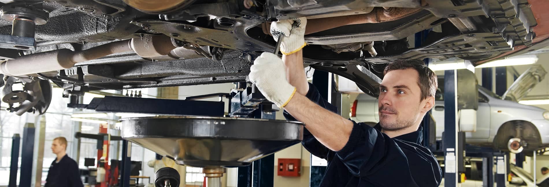 Service picture of technician working on the underside of car in service bay of raised cars