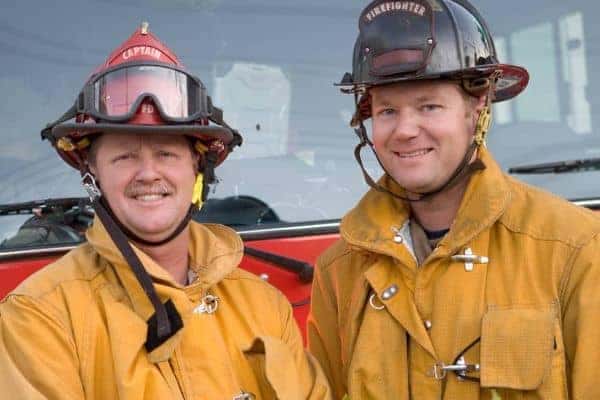 Two firemen standing in front of a firetruck