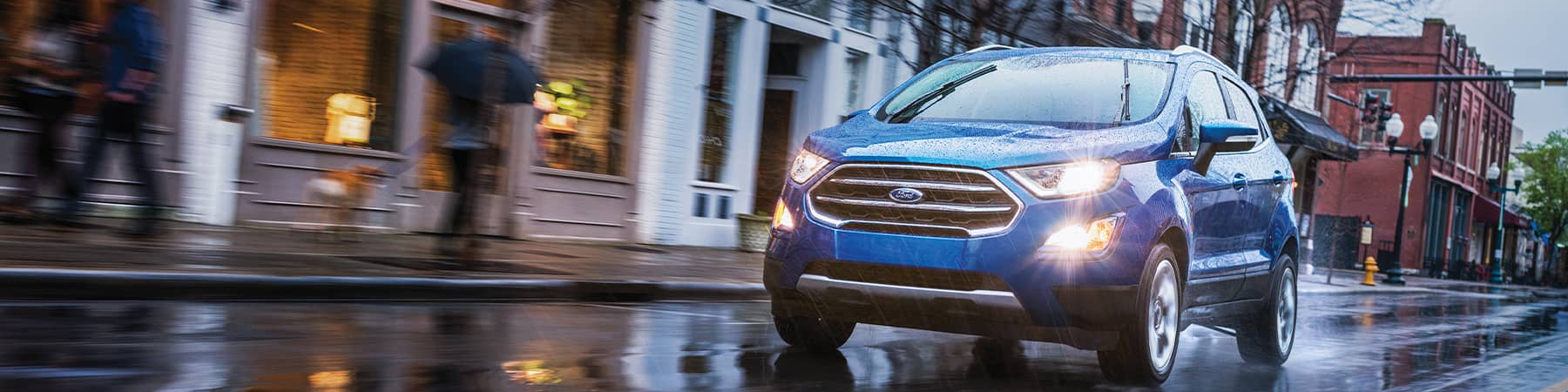 Blue 2021 Ford EcoSport driving on a rainy suburban town street