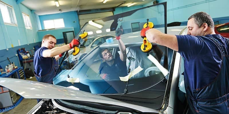 Certified technicians replacing windshield in damaged car