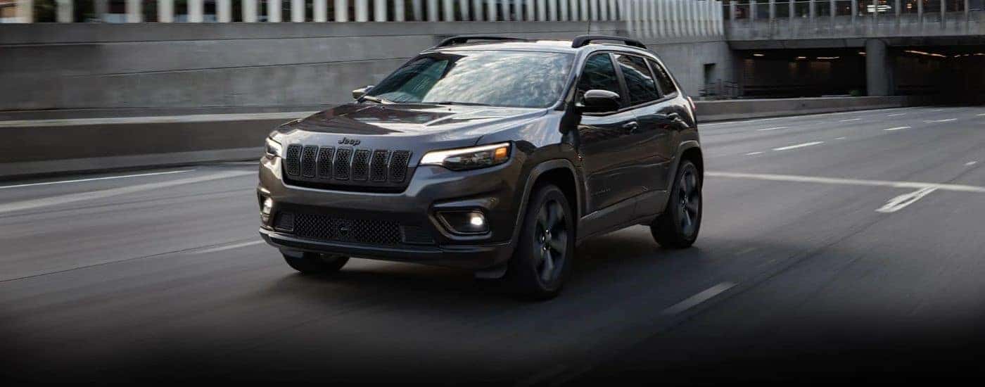 A dark grey 2023 Jeep Cherokee is shown driving on a city street.