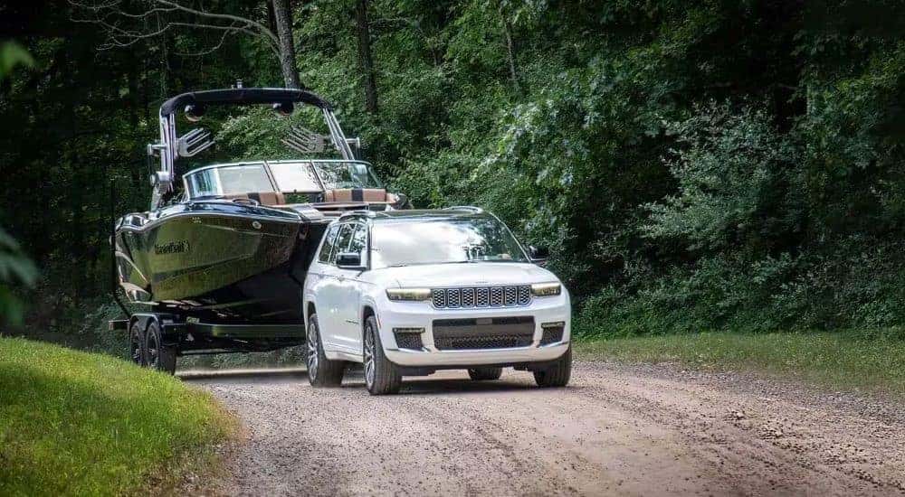 A white 2024 Jeep Grand Cherokee is shown towing a boat after leaving a Jeep dealer.