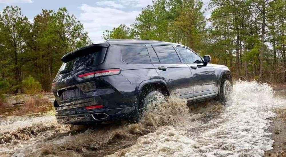 A blue 2024 Jeep Grand Cherokee is shown from the side driving though water.
