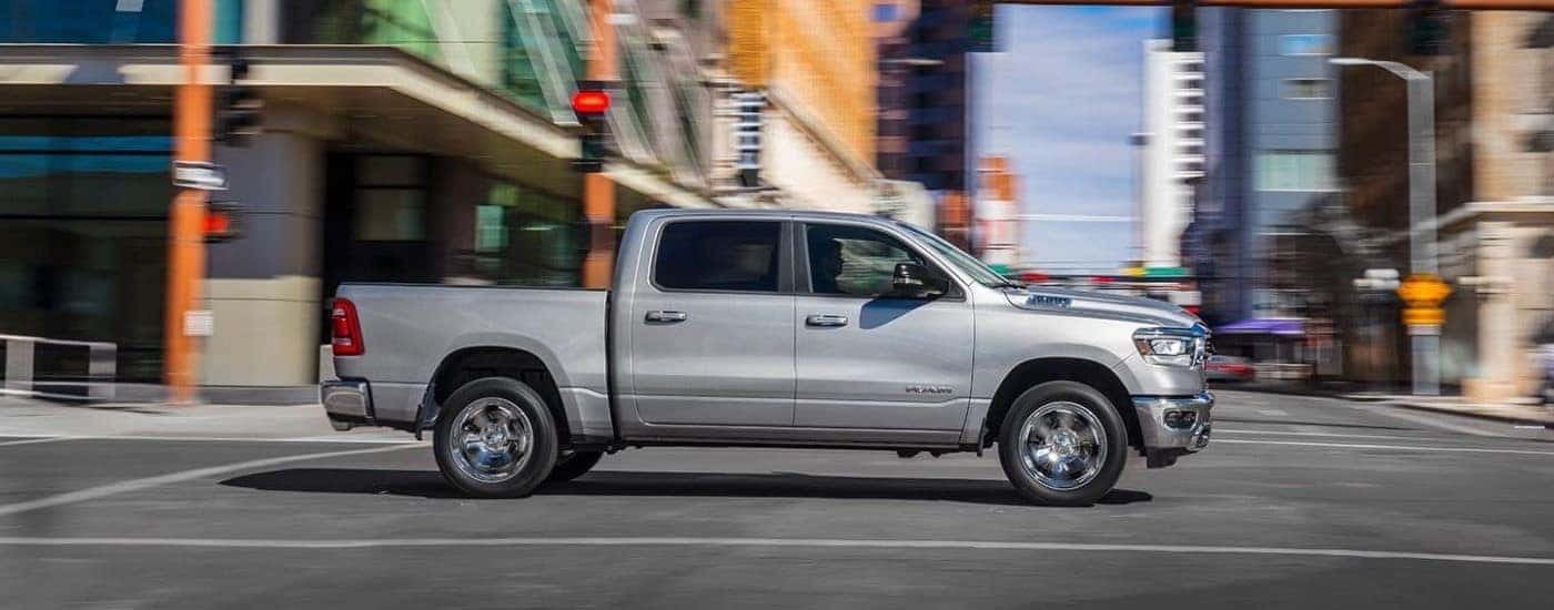 A silver 2019 Ram 1500 is shown from the side driving on a city street.