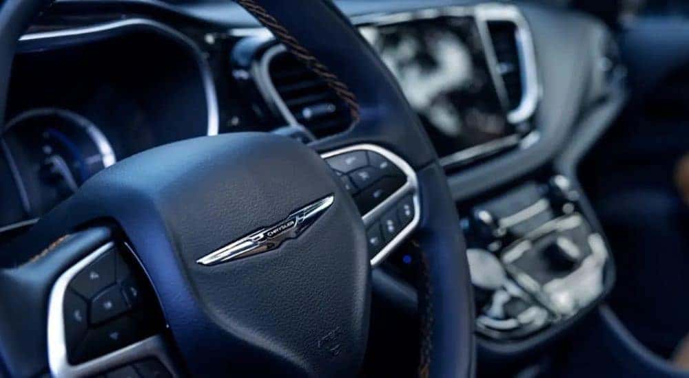 A close up shows the chrome Chrysler badge on the sterring wheel in a 2023 Chrysler Pacifica Hybrid.