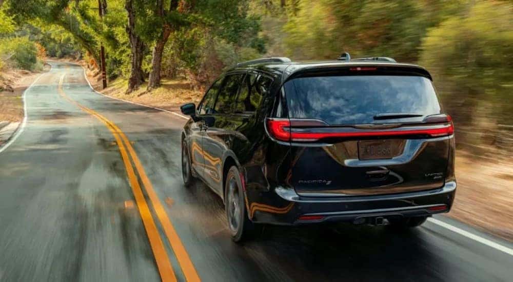 A black 2023 Chrysler Pacifica S Limited is shown driving on a tree-lined road.