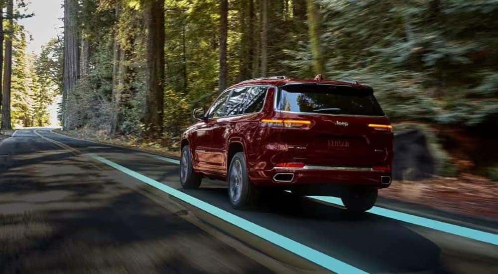 A maroon 2023 Jeep Grand Cherokee is shown driving on a tree-lined road after leaving a Jeep dealer.
