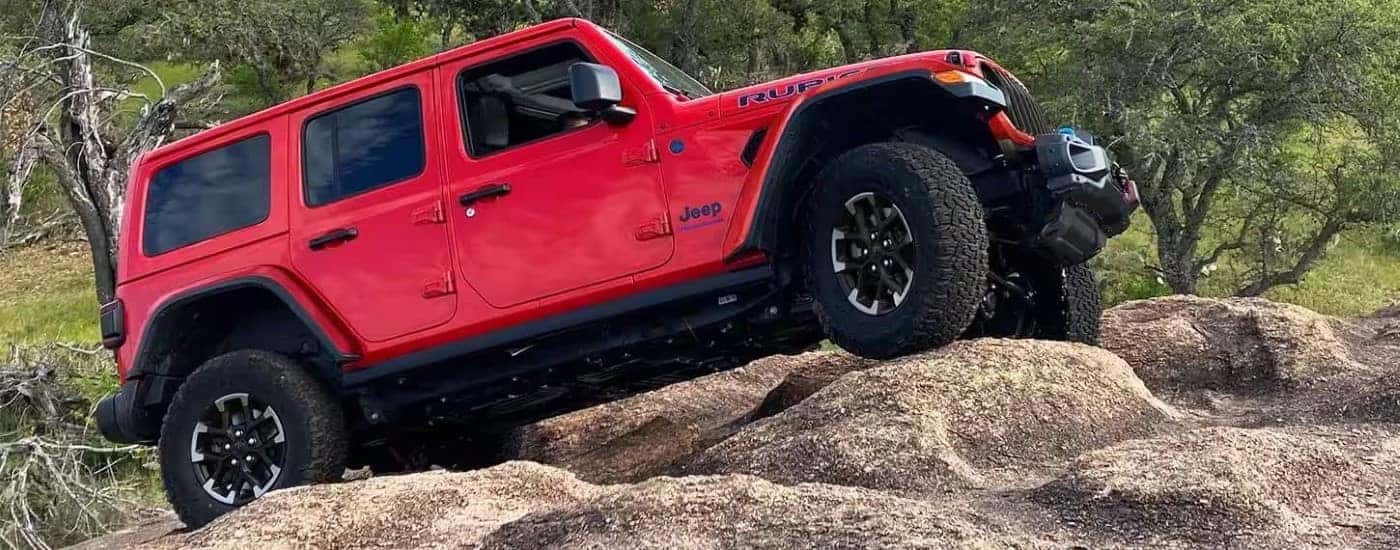 A red 2024 Jeep Wrangler 4xe Rubicon is shown off-roading after visiting a Jeep Wrangler dealer.