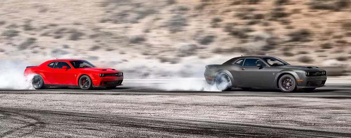 A red and a grey 2023 Dodge Challenger SRT Hellcat Widebody are shown doing burnouts.