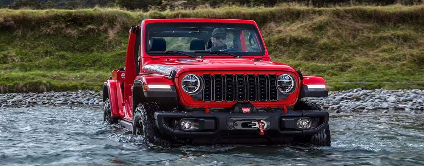 A red 2024 Jeep Wrangler Rubicon is shown from the front while fjording a river.