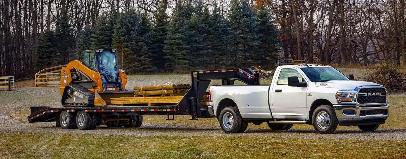 A white 2024 Ram 3500 is shown from the side while towing a skid-steer.