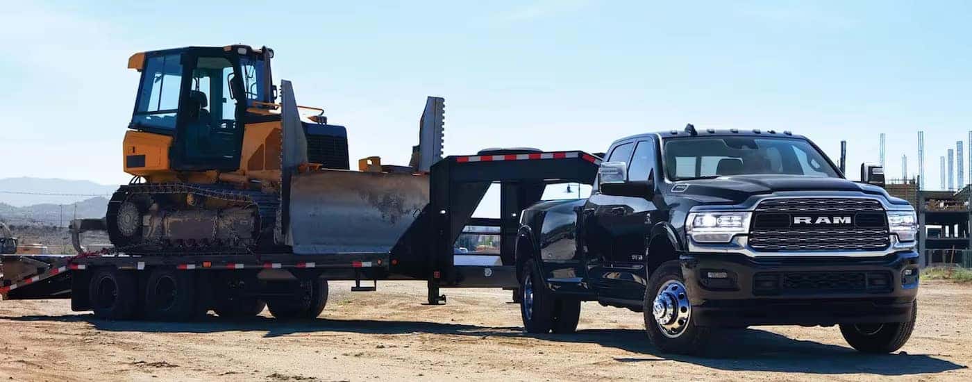 A black 2024 Ram 3500 for sale is shown from the front while towing a bulldozer.