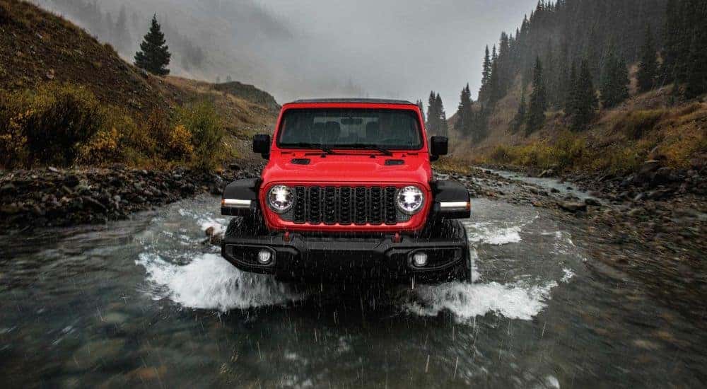A red 2024 Jeep Wrangle for sale is shown driving through a river.