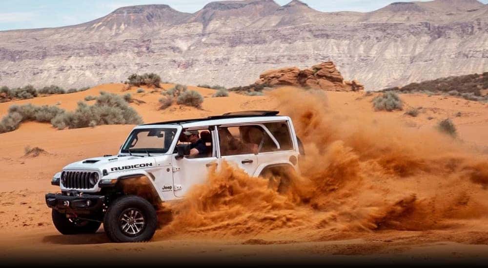 A white 2024 Jeep Wrangler Unlimited Rubicon is shown kicking up sand.