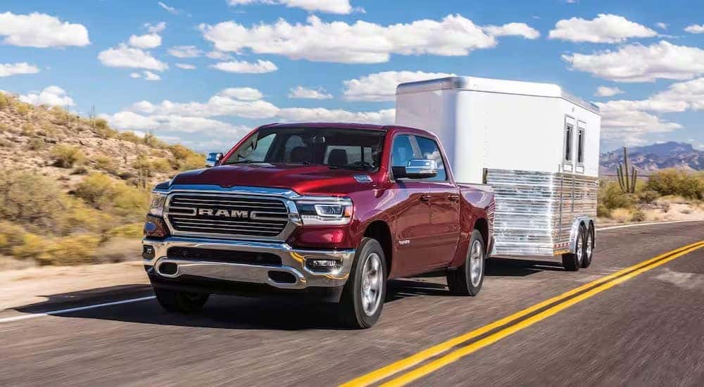 A red 2024 Ram 1500 is shown towing a trailer on a highway.