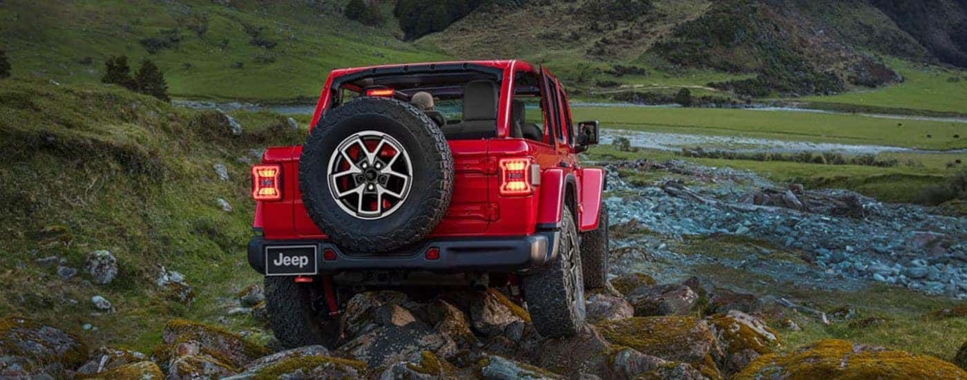 A rear view of a red 2024 Jeep Wrangler Unlimited driving off-road.