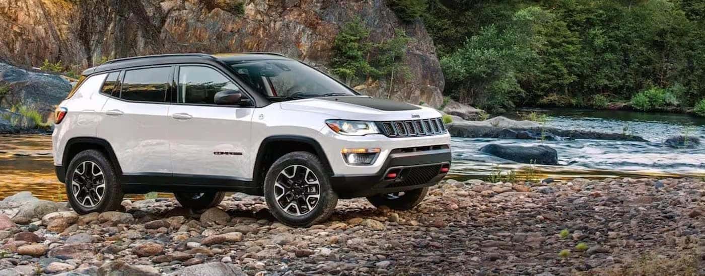 A white 2024 Jeep Compass Trailhawk parked by a river shore.