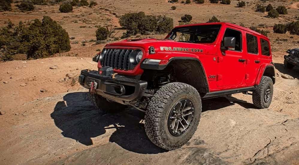 A red 2024 Jeep Wrangler Rubicon is shown driving off-road after viewing a Jeep Wrangler for sale near Huntsville.