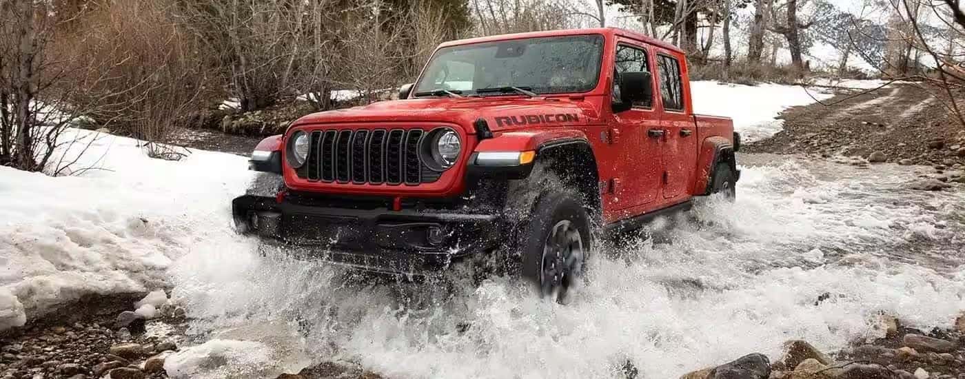 A red 2023 Jeep Gladiator Rubicon fording a shallow river.