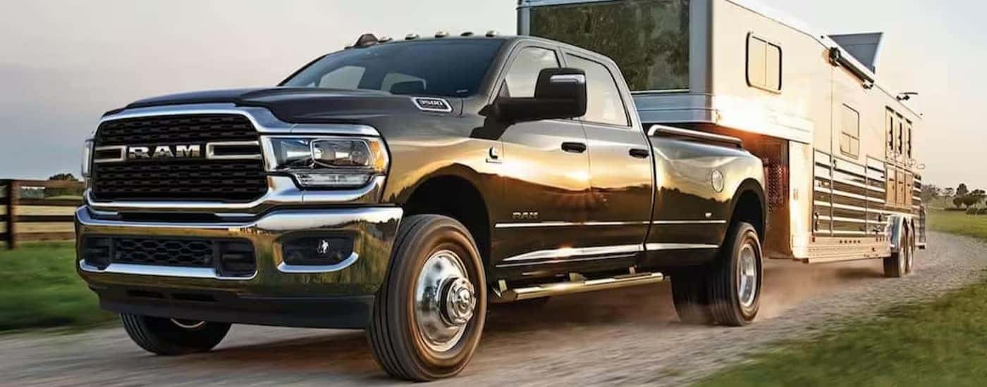 A black 2024 Ram 3500 is shown towing a trailer on a dirt road.